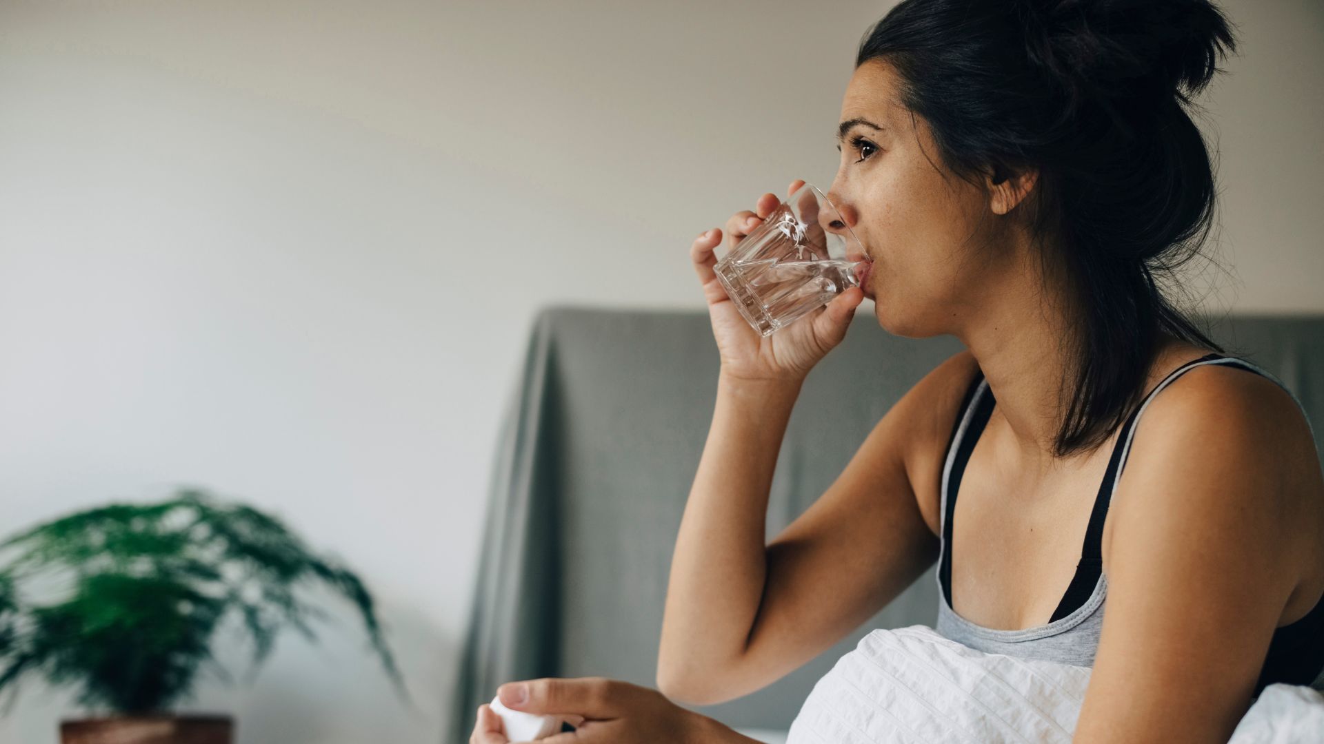 A woman is sitting on a bed drinking a glass of water.