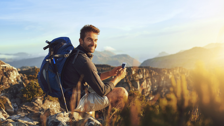 Young pedestrian man sitting on the ground and smiling at the camera with a phone in his hands