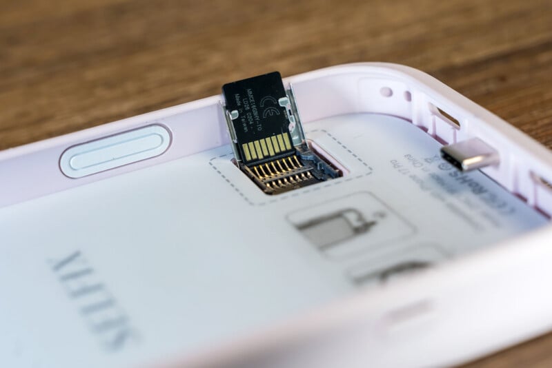 The closure of the microSD card inserted into the slot in the electronic device is white, and there are visible pins and pictures of the instructions printed on the machine.