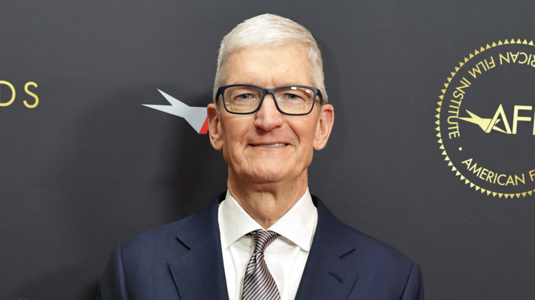 Tim Cook smiled, standing against a blue background.