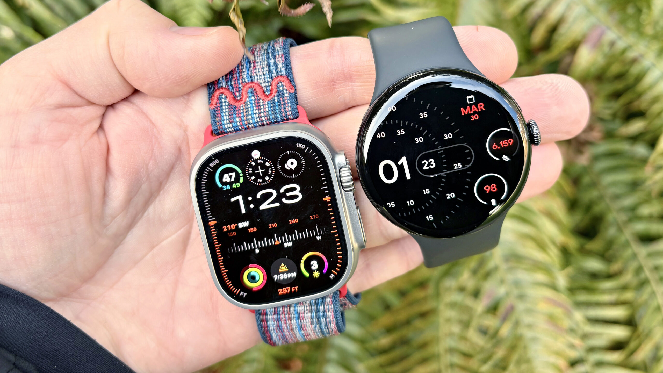 Close-up of the Apple Watch Ultra 3 and Google Pixel Watch 4 on the user's hand against a neutral colored background.