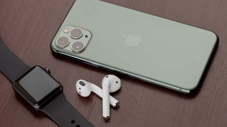 Apple Watch and two AirPods sitting next to Apple iPhone on wood