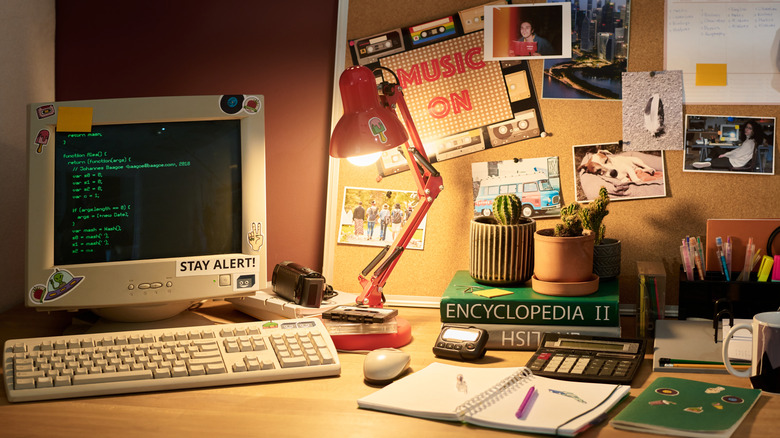 Old school desk chair with '90s style computer with books, office supplies, vintage digital cameras, and wall decor.